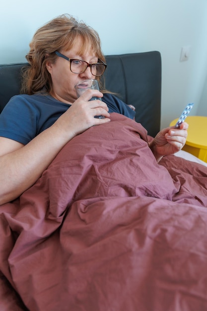 Foto zieke oude vrouw die thuis in bed ligt, voelt zich ziek, lijdt aan griep of verkoudheid, geneest met medicijnen