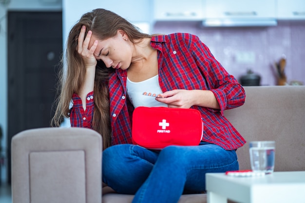 Zieke overstuur ongelukkige vrouw die lijdt aan hoofdpijn en migraine neemt medicijnen thuis. Medische EHBO-doos met pillen en pijnstillers tegen ziekten en pijnen