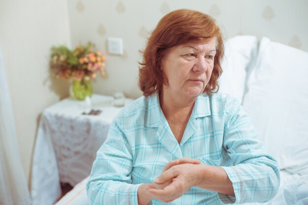 Zieke senior vrouw in bed in haar appartementen die de polsslag op haar hand neemt