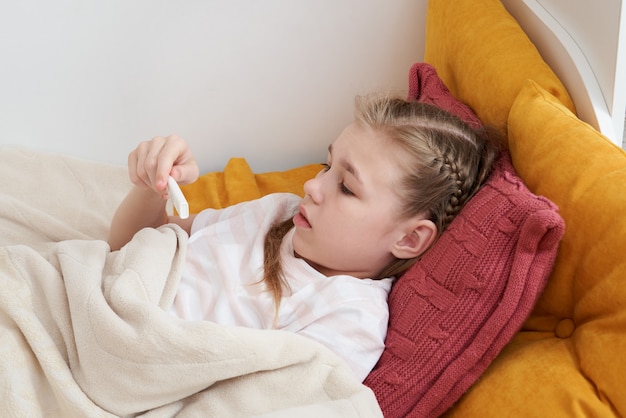 Zieke tiener die in bed legt en een thermometer bekijkt