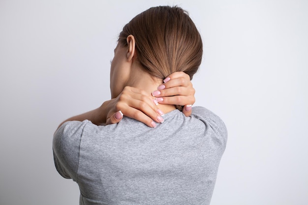 Zieke vrouw die lijdt aan een zere nek op een grijze achtergrond