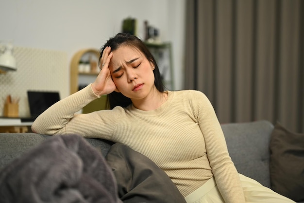 Zieke vrouw die op een bank zit met haar ogen dicht en haar hoofd aanraakt en lijdt aan sterke chronische hoofdpijn, migraine