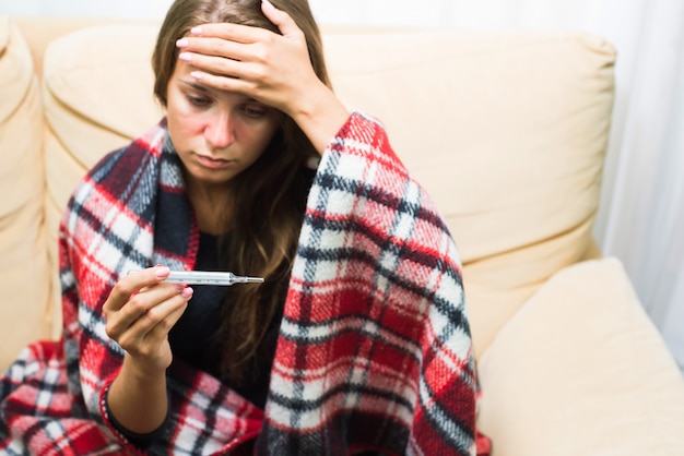 Zieke vrouw die thermometer bekijkt