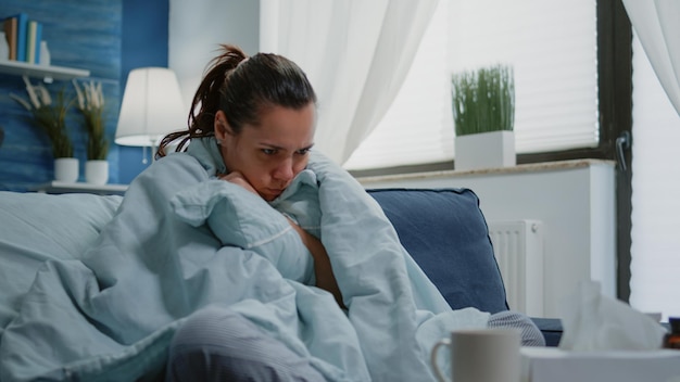 Foto zieke vrouw gewikkeld in een deken zit op de bank