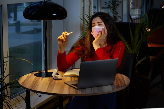 zieke vrouw met pillen en thermometer op een tafel werken op een laptop vanuit huis op quarantaine-isolatie.