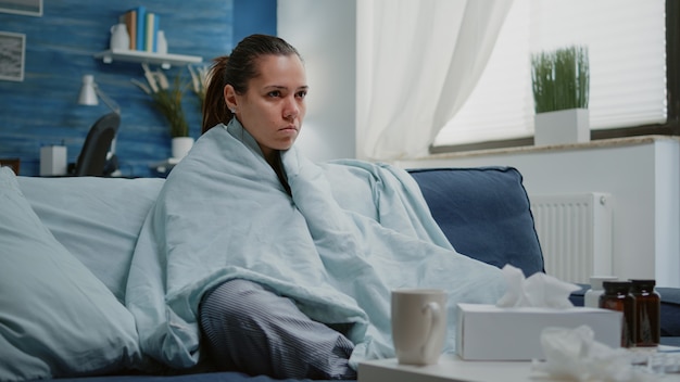 Foto zieke vrouw met seizoensgriep rillend in deken thuis