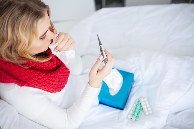 Zieke vrouw, vrouw met griepvirus liggend in bed, ze meet haar temperatuur met een thermometer