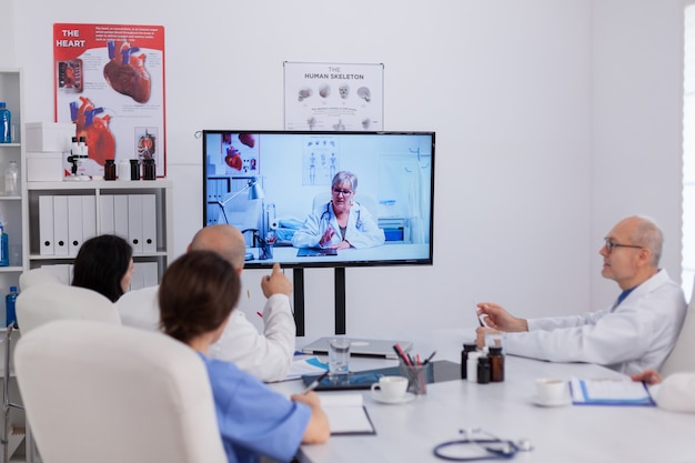 Ziekenhuisteamwerk in gesprek met neuroloog senior arts tijdens online videogesprek teleconferentie over ziektesymptoom dat pillenbehandeling uitlegt. Neurologen team werken in vergaderruimte