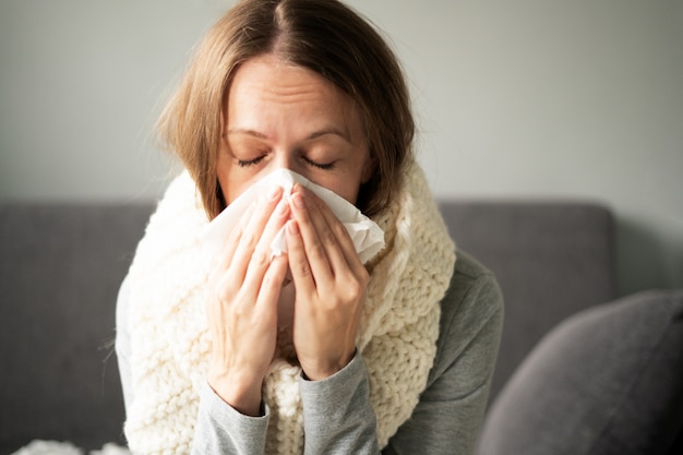 Ziekte. Thuisbehandeling. Een vrouw is thuis ziek, loopneus en griep. Warm gekleed en bedekt met een deken.