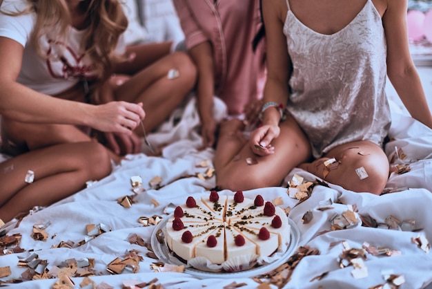 Ziet er heerlijk uit. Close-up van vier jonge vrouwen in pyjama die zich klaarmaken om cake te eten tijdens een slaapfeestje