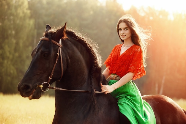 Zigeunermeisje rijdt in de zomer op een paard in een veld. een vrouw met lang haar streelt en streelt een paard dat in het groene gras staat