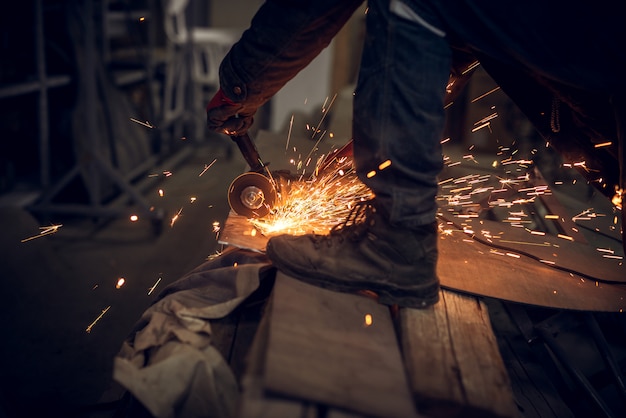 Zij dichte omhooggaande mening van stoffenarbeider die met elektrisch molenhulpmiddel aan een staalstructuur werken in de fabriek terwijl vonken het vliegen.