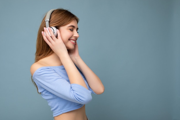 Zij-profielfoto van mooie positieve glimlachende jonge blonde vrouw die blauwe crop top draagt