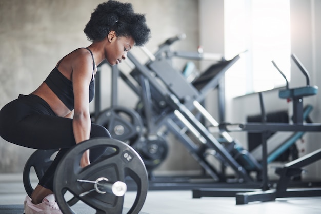 Zijaanzicht. Afro-Amerikaanse vrouw met krullend haar en in sportieve kleding hebben fitnessdag in de sportschool