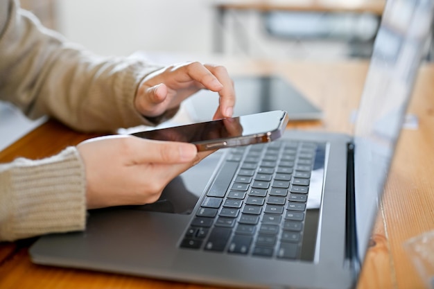 Zijaanzicht Aziatische vrouw met behulp van haar smartphone aan haar bureau voor de laptopcomputer