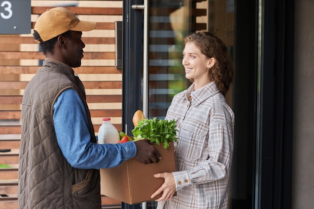 Zijaanzicht bezorger die doos met verse boodschappen overhandigt aan vrouw