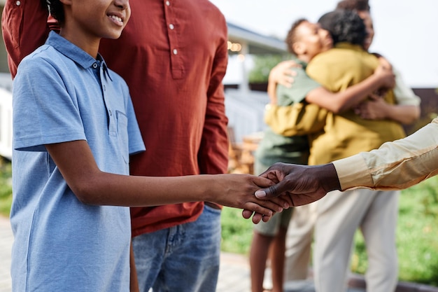 Foto zijaanzicht close-up van jonge afro-amerikaanse jongen die handen schudt met familielid tijdens zomerfeest