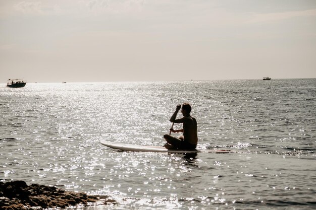 Zijaanzicht foto van een man die zwemt en ontspant op het sup board sportieve man in de zee op de stand