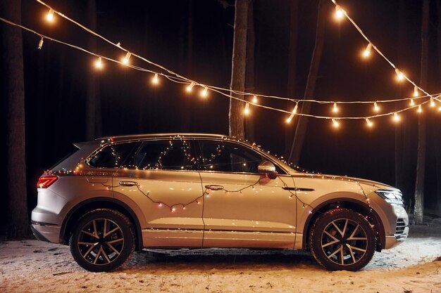 Zijaanzicht Moderne zilverkleurige auto geparkeerd in het bos met vakantiedecoratie