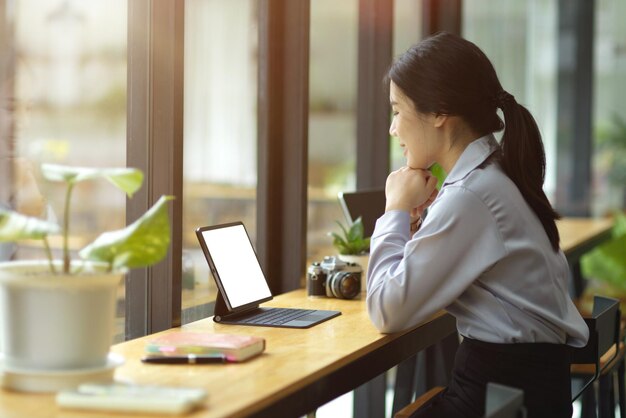 Zijaanzicht, mooie jonge aziatische zakenvrouw die op tablet werkt, op het scherm kijkt, denkt om online inhoud te creëren, zit in café.