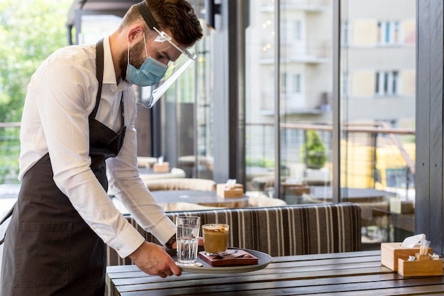 Foto zijaanzicht ober met masker serveren