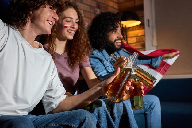 Zijaanzicht op opgewonden vrienden die flessen bier rammelen tijdens sportwedstrijd op tv, juichen voor het beste amerikaanse team, anticiperend op het doel. focus op lachende kerel