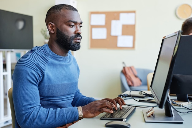 Zijaanzicht portret van bebaarde zwarte man die laptop op kantoor gebruikt tijdens het programmeren van software