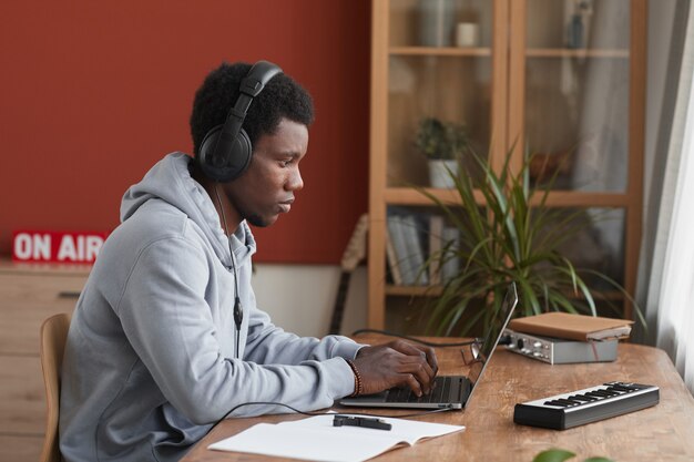 Zijaanzicht portret van jonge Afro-Amerikaanse muzikant met behulp van laptop tijdens het componeren van muziek thuis, kopieer ruimte
