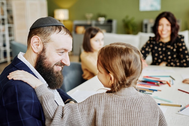 Zijaanzicht portret van lachende joodse man spelen met kinderen thuis met familie op achtergrond