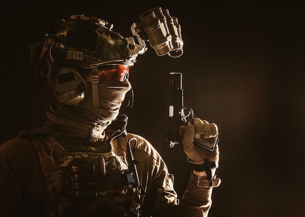 Zijaanzicht portret van leger soldaat moderne strijder speciale krachten vechter in helm nachtzicht apparaat radio hoofdtelefoon identiteit achter masker gewapende dienst pistool low key studio shoot
