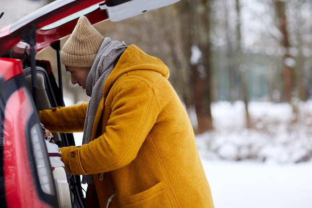 Zijaanzicht portret van man auto kofferbak openen in de winter tijdens het reizen voor vakantie kopieer ruimte