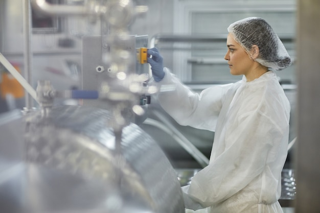 Zijaanzicht portret van vrouwelijke werknemer die op de knop drukt terwijl ze machine-eenheden bedient in een fabriek voor schone voedselproductie, kopieer ruimte