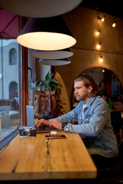 Zijaanzicht portret van zelfverzekerde blanke man in spijkerjasje bezig met laptop, gericht op werk, zijaanzicht portret. Hipster Man geniet van werken aan freelance, denken