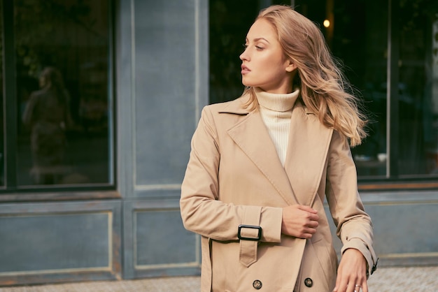 Zijaanzicht van aantrekkelijk blond meisje in trenchcoat die zelfverzekerd wegkijkt op straat