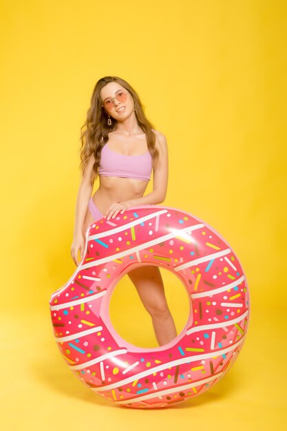 Zijaanzicht van aantrekkelijke jonge vrouw in badmode trendy zonnebril met donutvormige zwemring