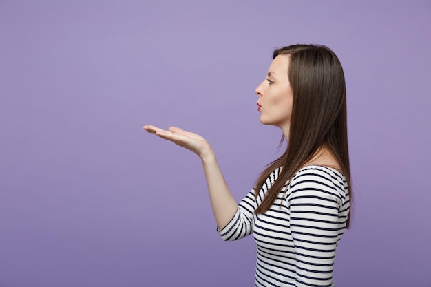 Zijaanzicht van aantrekkelijke jonge vrouw meisje in casual gestreepte kleding poseren geïsoleerd op violet paarse achtergrond studio portret. mensen levensstijl concept. bespotten kopie ruimte. blazende luchtkus verzenden.