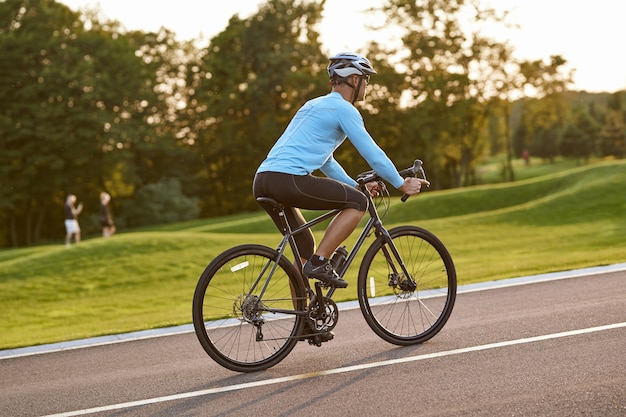 Foto zijaanzicht van atletische man in sportkleding die fietst langs een weg in stadspark