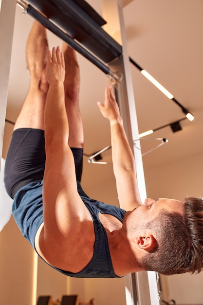 Zijaanzicht van blootsvoets mannelijke atleet liggend op pilates hervormer en het uitvoeren van buikspieroefeningen tijdens fitnesstraining pilates man concept