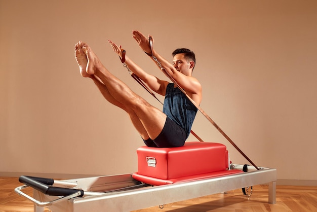 Zijaanzicht van blootsvoets mannelijke atleet liggend op pilates hervormer en het uitvoeren van buikspieroefeningen tijdens fitnesstraining Pilates man concept