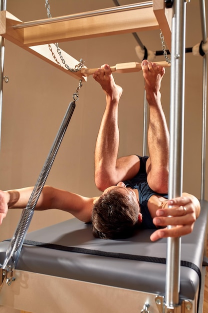 Zijaanzicht van blootsvoets mannelijke atleet liggend op pilates hervormer en het uitvoeren van buikspieroefeningen tijdens fitnesstraining Pilates man concept