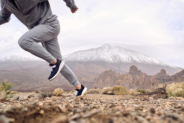 Zijaanzicht van crop anonieme mannelijke reiziger in sportkleding die snel rent op rotsachtige grond tegen berg Teide bedekt met sneeuw in Tenerife Canarische Eilanden Spanje