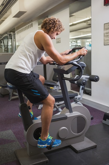 Zijaanzicht van de mens die op hometrainer uitwerkt bij gymnastiek