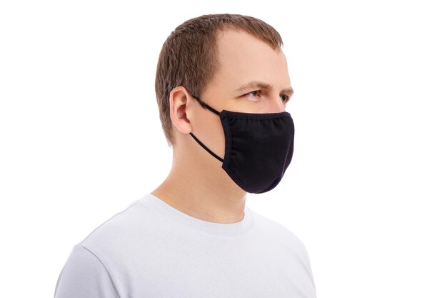 Zijaanzicht van de mens in witte t-shirt die zwart medisch gezichtsmasker draagt dat op witte achtergrond wordt geïsoleerd