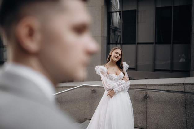 Zijaanzicht van de vrouw, gekleed in een witte trouwjurk, poserend buitenshuis Paar trouwen bruid sloot haar ogen lachende bruidegom staande Concept van huwelijk en liefde