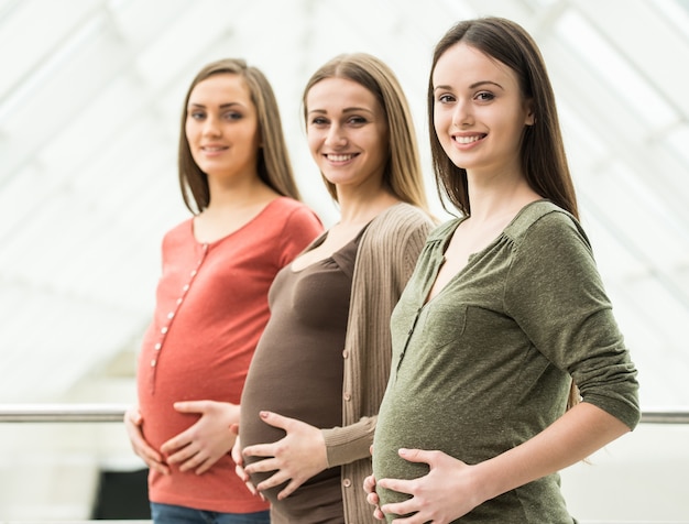 Zijaanzicht van drie glimlachende zwangere vrouwen.