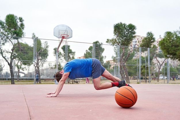 Zijaanzicht van een atletische jonge man die push-ups doet met een basketbalveld