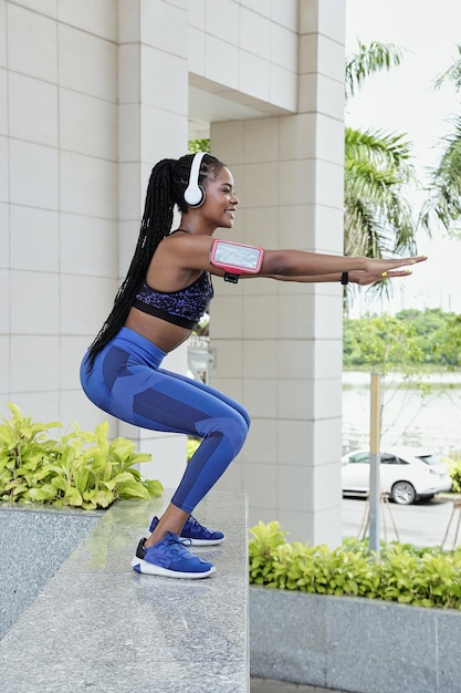 Zijaanzicht van een fitte jonge Afro-Amerikaanse sportvrouw die buiten squats doet, terwijl ze aan haar bilspieren en dijen werkt