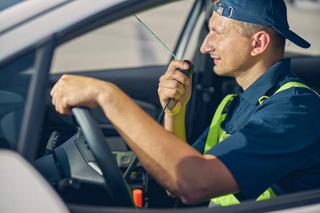 Zijaanzicht van een gefocuste blanke voertuigbestuurder die een radiozendontvanger in zijn auto gebruikt