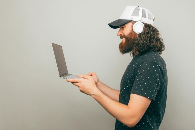 Zijaanzicht van een gekrulde man die een koptelefoon draagt en een geopende laptop vasthoudt