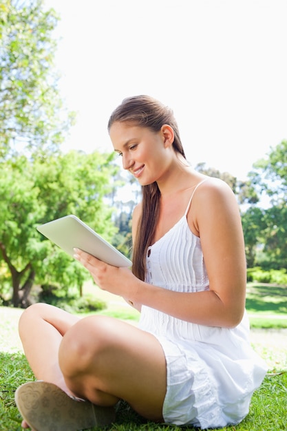 Zijaanzicht van een glimlachende vrouw die een tabletcomputer in het park met behulp van